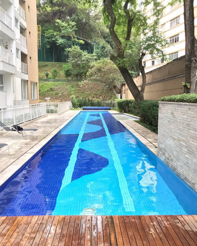 Piscina de raia com azulejos em tons de azul e água cristalina, ao lado de deck de madeira