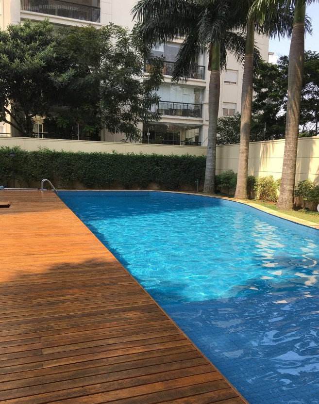 Piscina curva com deck de madeira e palmeiras
