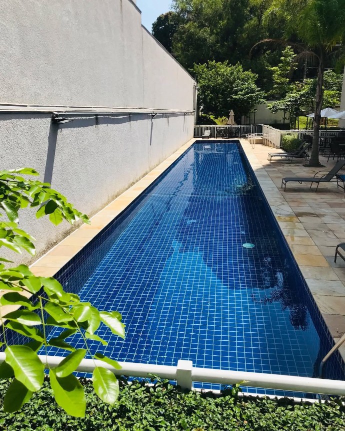 Piscina estreita de condomínio com pastilhas azuis e espaço de descanso